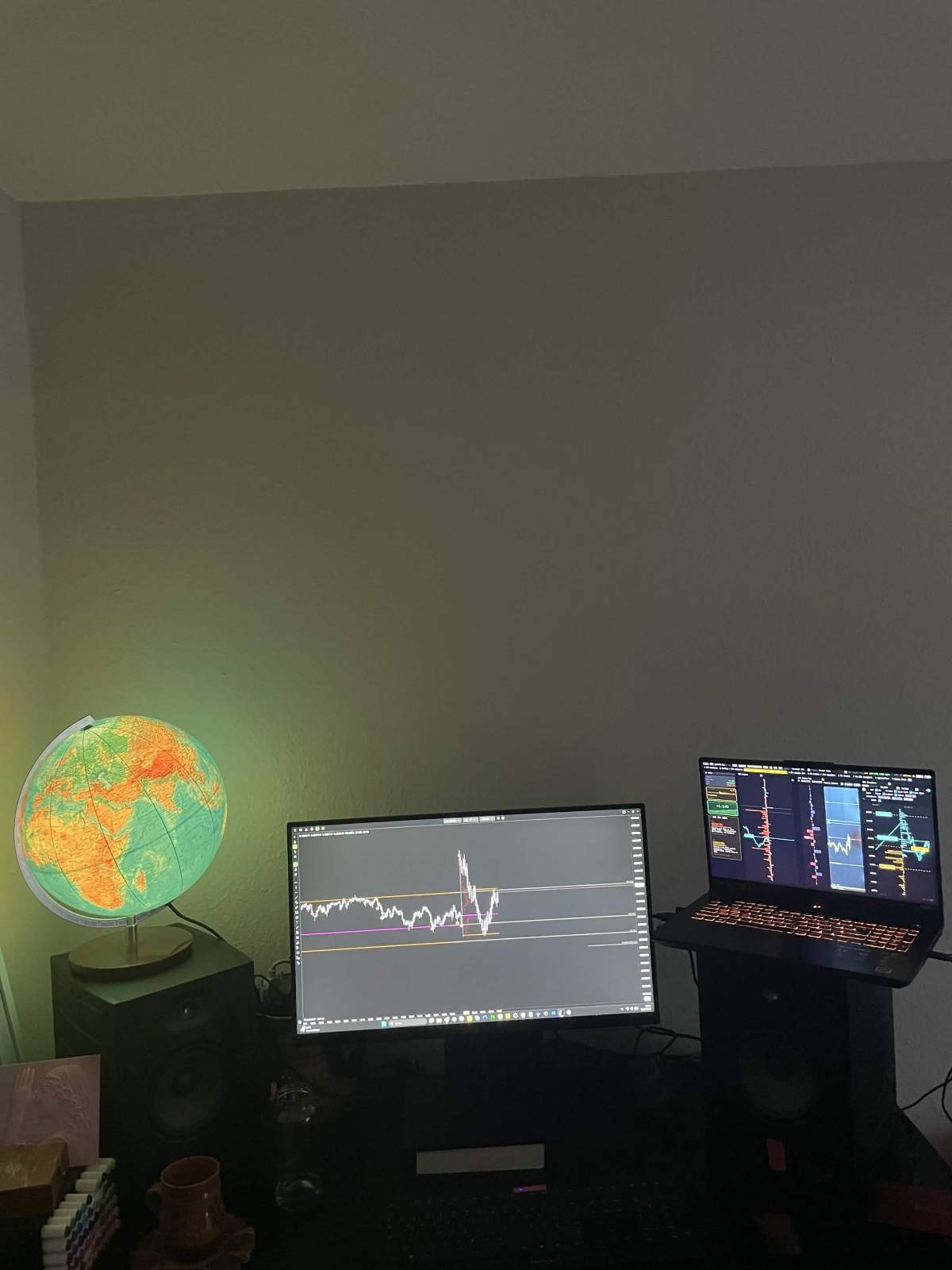 Desktop and laptop trading setup beside an illuminated globe